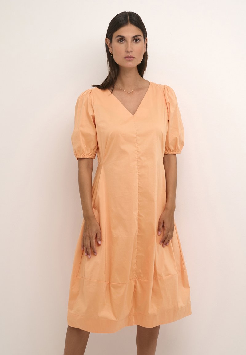 Vestido de algodón melocotón con mangas abullonadas, escote en V y falda fruncida. Textura suave, a la altura de la rodilla, con una costura central en el frente.