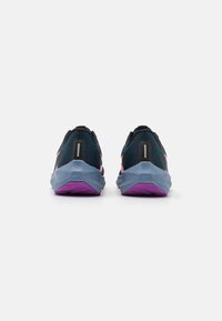 Un paio di scarpe da corsa Nike blu scuro e viola viste da dietro, evidenziando le suole intermedie testurizzate e le strisce riflettenti sul tallone.