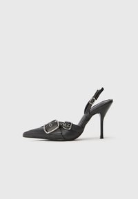 Stiletto cu vârf ascuțit, de culoare neagră, cu catarame duble argintii și o brățară pentru gleznă, expus pe un fundal alb simplu.