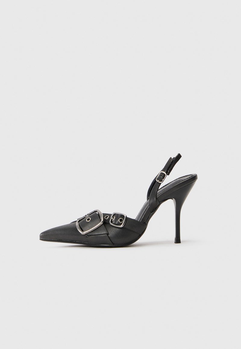 Stiletto cu vârf ascuțit, de culoare neagră, cu catarame duble argintii și o brățară pentru gleznă, expus pe un fundal alb simplu.