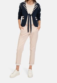 Marinblå kofta med randig kant och knytband, matchad med ljusbeiga byxor och vita sneakers. Mjuka material, avslappnad passform, avslappnad design.