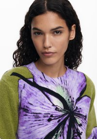 Knit sweater featuring a floral design in purple and green, with a round neckline and a soft texture. Black accents highlight the flower.