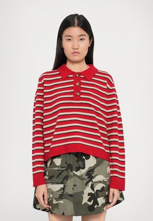 Sweater listrado em vermelho e bege com gola e quatro botões de madeira, combinado com uma saia com padrão de camuflagem e bolsos.