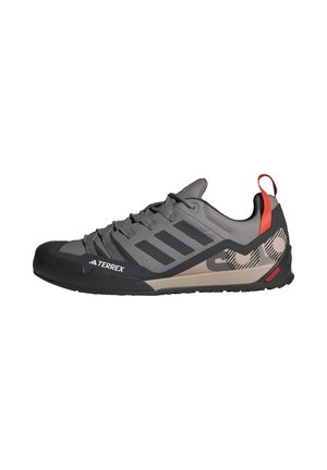 Chaussure de randonnée Adidas Terrex basse grise et noire avec semelle beige, rayures noires et languette rouge au talon.