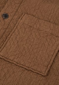 Gestepptes braunes Gewebe mit Rautensteppung, das eine rechteckige Tasche und einen dunkelbraunen Knopf aufweist.