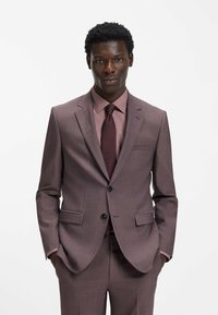 Hellvioletter Anzug mit strukturierter Oberfläche, ausgestattet mit einem Reverskragen, zwei Taschen und einem Ein-Knopf-Verschluss, kombiniert mit einer passenden Krawatte.