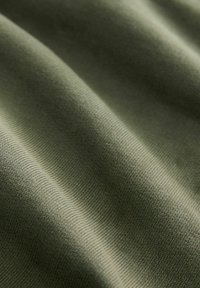 Olijfgroene stof met een zachte textuur, kenmerkend door subtiele ribbels en lichte plooien, wat duidt op een lichtgewicht en flexibele kwaliteit.