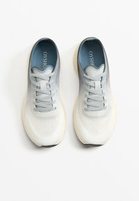Könnyű sportcipők szürke és fehér hálós anyagból, sima talppal, fűzőrendszerrel és párnázott kék talpbetéttel.