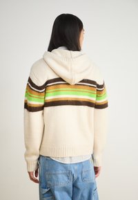 Sweatshirt cu glugă în crem, cu dungi maro, verzi și albe pe spate. Textură tricotată, mansete și tiv cu nervuri, croială lejeră.