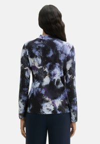 Dlouhý rukáv top v texturované, elastické tkanině. Vyznačuje se odvážným modrým, černým a bílým abstraktním vzorem s zakřiveným výstřihem.