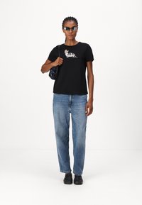 Zwarte t-shirt met een grafisch ontwerp van een kleurrijk dier, gecombineerd met lichtblauwe wijde jeans en zwarte schoenen. Accessoire: donkere handtas.