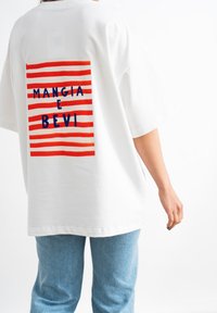 T-shirt bianca oversize con una grafica a righe rosse e bianche sul retro e testo blu che recita "MANGIA E BEVI."