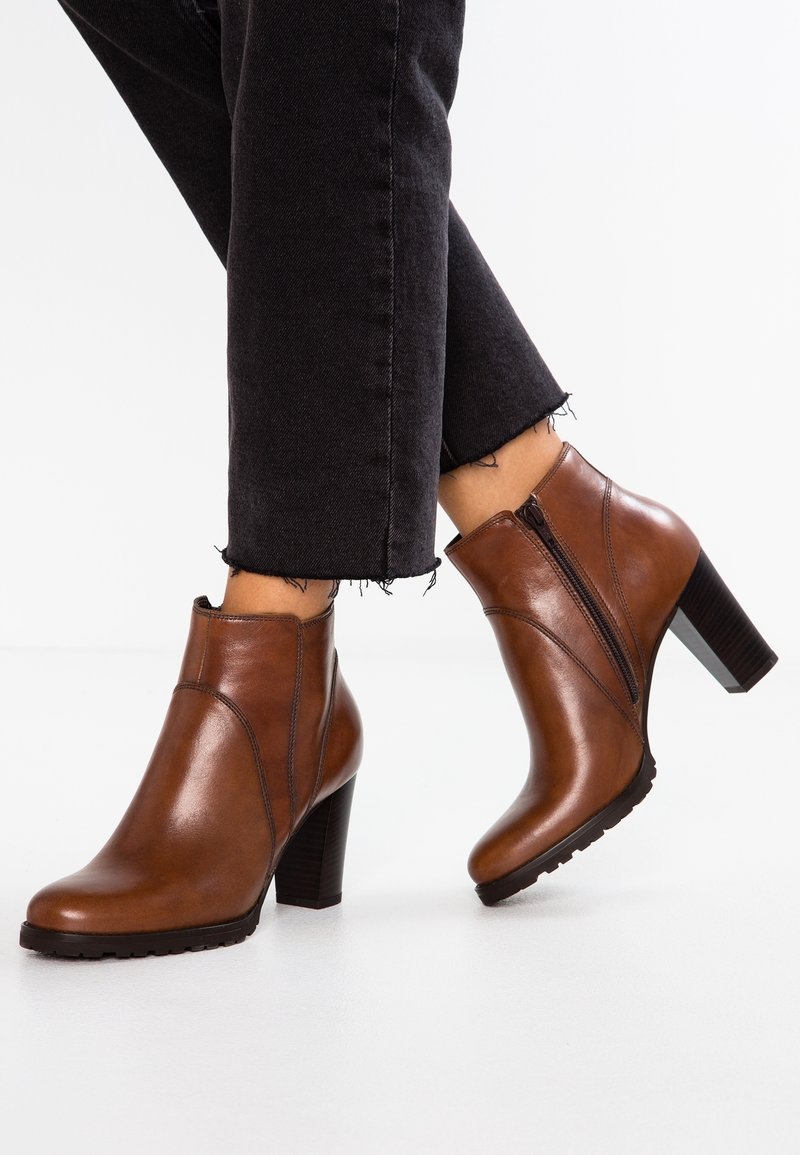 Bottines en cuir marron avec fermeture éclair latérale et talons blocs hauts portées avec un jean noir à ourlet effiloché.