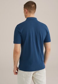 Temno modra polo majica s kratkimi rokavi, ovratnikom in teksturirano tkanino. Ima stranske razpoke na robu in gladko površino.