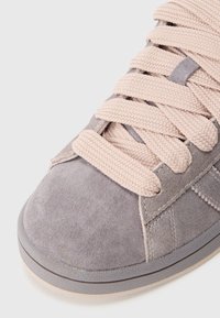 Sive semiš superge s debelimi, teksturiranimi svetlo roza vezalkami, oblazinjeno jezičkom in sivim gumijastim podplatom z gladko površino.