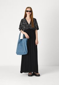 Rochie maxi neagră cu broderie florală albă, asortată cu o geantă de tote din denim albastru deschis și sandale negre cu platformă.