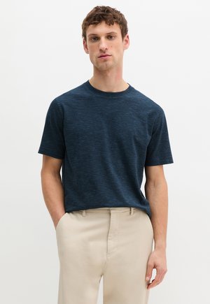 Marineblaue kurze T-Shirt mit einer strukturierten, gestreiften Musterung; runder Ausschnitt; getragen mit beigen Hosen.