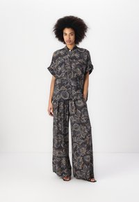 Twee-delig outfit met een kortmouw overhemd met knopen en wijde broek in zwart met een bloemenpatroon in room- en goudtinten.