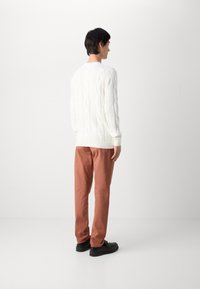 Valkoinen neulepusero, jossa on raidoitetut hihansuut, yhdistettynä vaalean ruosteenvärisiin housuihin ja mustiin kenkiin, nähtynä takaa. Tasainen pinta.