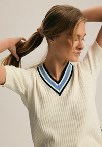 Biały sweter z prążkowanej dzianiny z dekoltem w kształcie litery V, jednocześnie z niebieskimi i czarnymi paskami, krótkimi rękawami oraz teksturowanym wykończeniem.