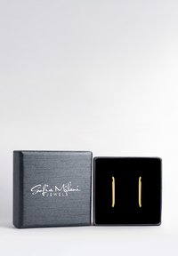 Goldfarbene Ohrringe in einer grau gepolsterten Box mit schwarzem Samt ausgelegt. Die Box hat eine strukturiert Oberfläche und ein weißes Logo auf dem Deckel.
