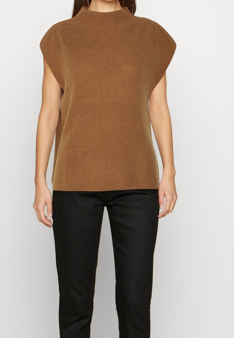 Bruine gebreide top met een hoge hals, kapmouwen en een gestructureerde silhouet. Gecombineerd met zwarte slim-fit broek.