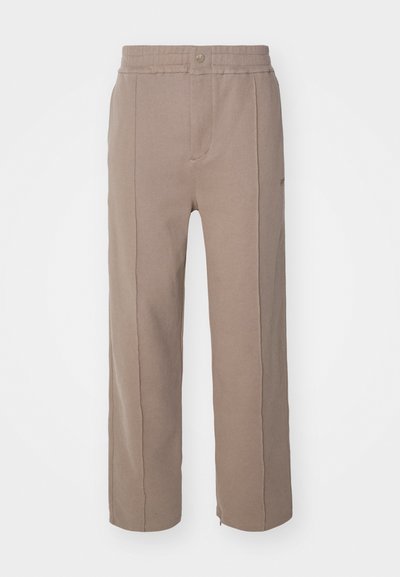 Hnědé široké kalhoty vyrobené z měkké, strukturované tkaniny. Mají stahovací pás, zapínání na knoflík a boční švy.