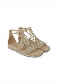Sandali beige con un design intagliato e decorazioni intricate. Sole interno liscio, tacco piatto, cinturino regolabile alla caviglia e punta rotonda.