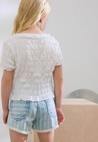 Witte, textuurgegeven top met korte mouwen en een gerimpelde zoom, gecombineerd met lichtblauwe, gestreepte denimshorts met rafelende randen en achterzakken.
