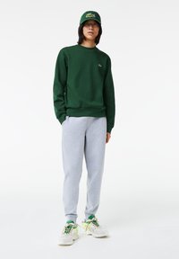 Grøn crewneck sweatshirt, grå sweatpants og hvide sneakers med grønne detaljer. Har et enkelt design med broderet logo på sweatshirt'en.