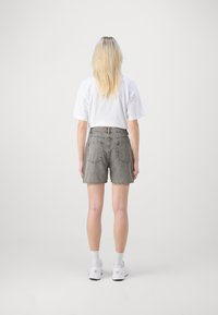 Shorts en denim gris à taille haute, avec ourlet roulé et deux poches arrière. Associés à un t-shirt blanc court et des baskets blanches.