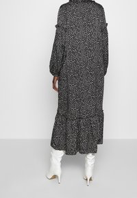 Robe midi à pois noir et blanc avec de longues manches bouffantes et un ourlet en couches. Portée avec des bottes à talons blanches, mettant en avant la texture et le mouvement.