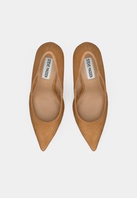 Ζευγάρι σουέντ μπεζ μπαλαρίνες με μυτερή μύτη και ετικέτες Steve Madden στο εσωτερικό, σε λευκό φόντο, από ψηλά.