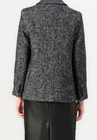 Schwarz-weiß gemusterter Wollblazer im Fischgratmuster mit Reverskragen und geknöpften Manschetten, kombiniert mit einem schwarzen Lederrock.