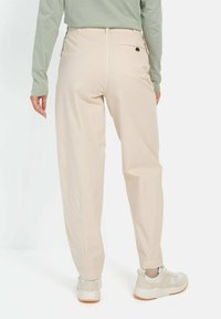 Beige bukser med en afslappet pasform, der har en baglomme med en knapdetalje, sammen med lyse sneakers.
