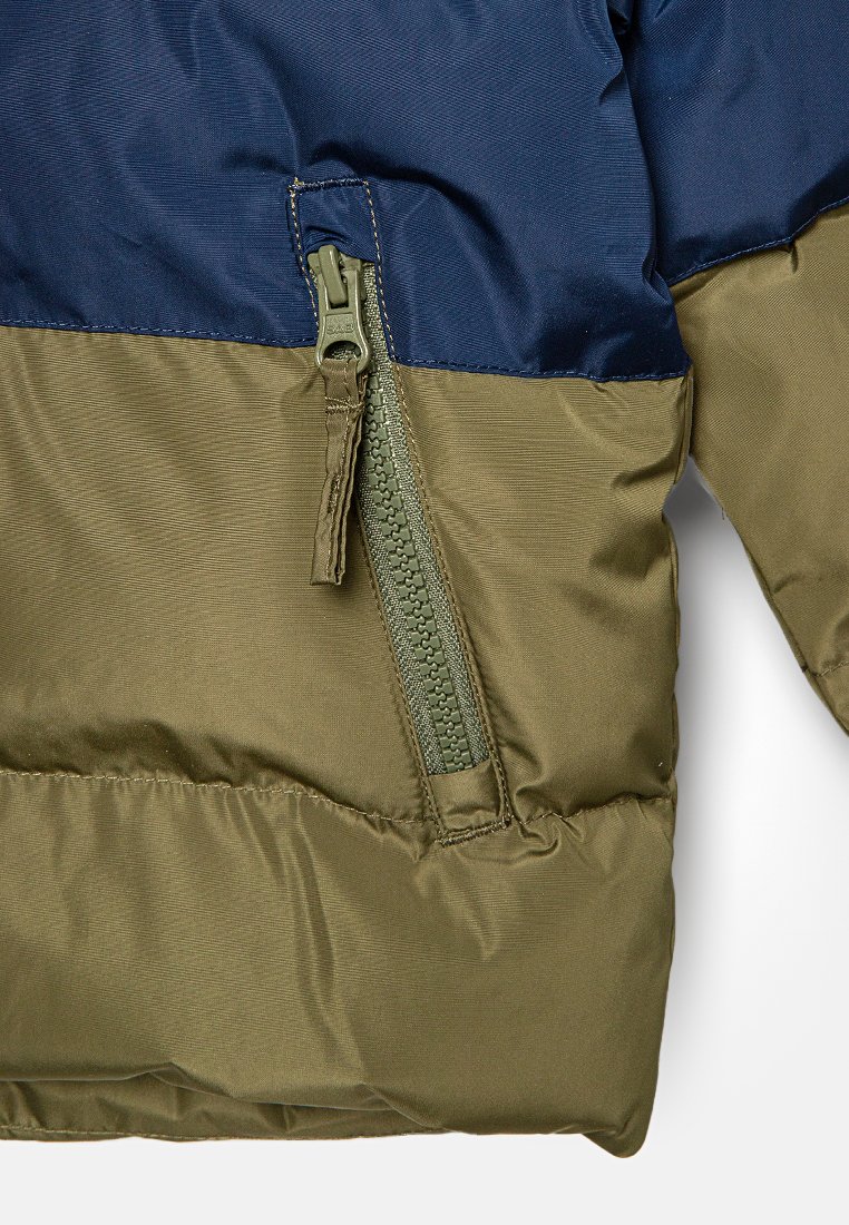 Veste rembourrée avec une section supérieure bleu marine et une section inférieure olive. Dotée d'une fermeture éclair verte et d'une texture lisse et brillante.
