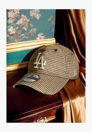 Bruine houndstooth pet met LA-logo, verstelbare band en zachte stoftextuur. Het label toont maat- en merkinformatie.