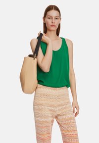 Beige textured tote bag with a black woven handle, paired with a green tank top and patterned, colorful wide-leg pants.