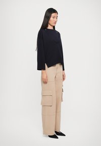 Maglione blu navy oversize con scollo allungato e dettagli a intaglio, abbinato a pantaloni cargo larghi beige con grandi tasche. Ballerine nere a punta.