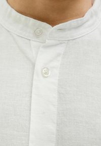 Camicia bianca in lino con colletto a banda, chiusura a un solo bottone e tessuto testurizzato con un delicato motivo di intreccio.