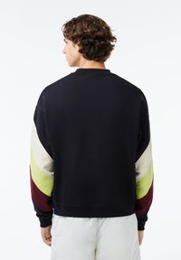 Sudadera tipo pullover en azul marino con mangas a bloques de color en beige, verde y burdeos. Tejido suave, cuello y puños acanalados.