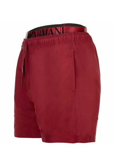 Bañador rojo para hombre con cintura elástica, cordón, bolsillo lateral y cinturilla negra y roja con la marca Armani parcialmente visible.