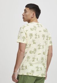 Gul t-skjorte i bomull med grønt jungle-tema print, med palmer og planter, rund halsutskjæring og korte ermer.