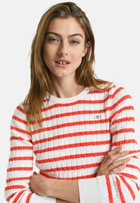 Rot-weißer gestreifter Strickpullover mit gerippter Textur und langen Ärmeln. Hat ein kleines Logodetail auf der Brust.