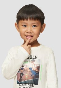 Langarm-Creme-T-Shirt mit einem Grafikmotiv eines Jungen und einem Dinosaurier auf einem Basketballplatz, mit dem Text "COURTSIDE CHAMPIONS" in fetter Schrift.