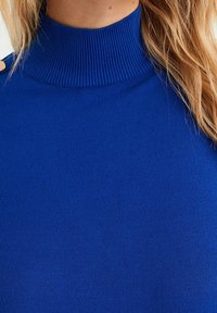 Blå, rullkragetröja med ett nära sittande design. Har axelknappar och en slät textur. Tillverkad av ett elastiskt material.