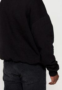 Sudadera negra con un corte relajado, hombros caídos y puños acanalados, combinada con jeans gris oscuro con un diseño de cinco bolsillos.