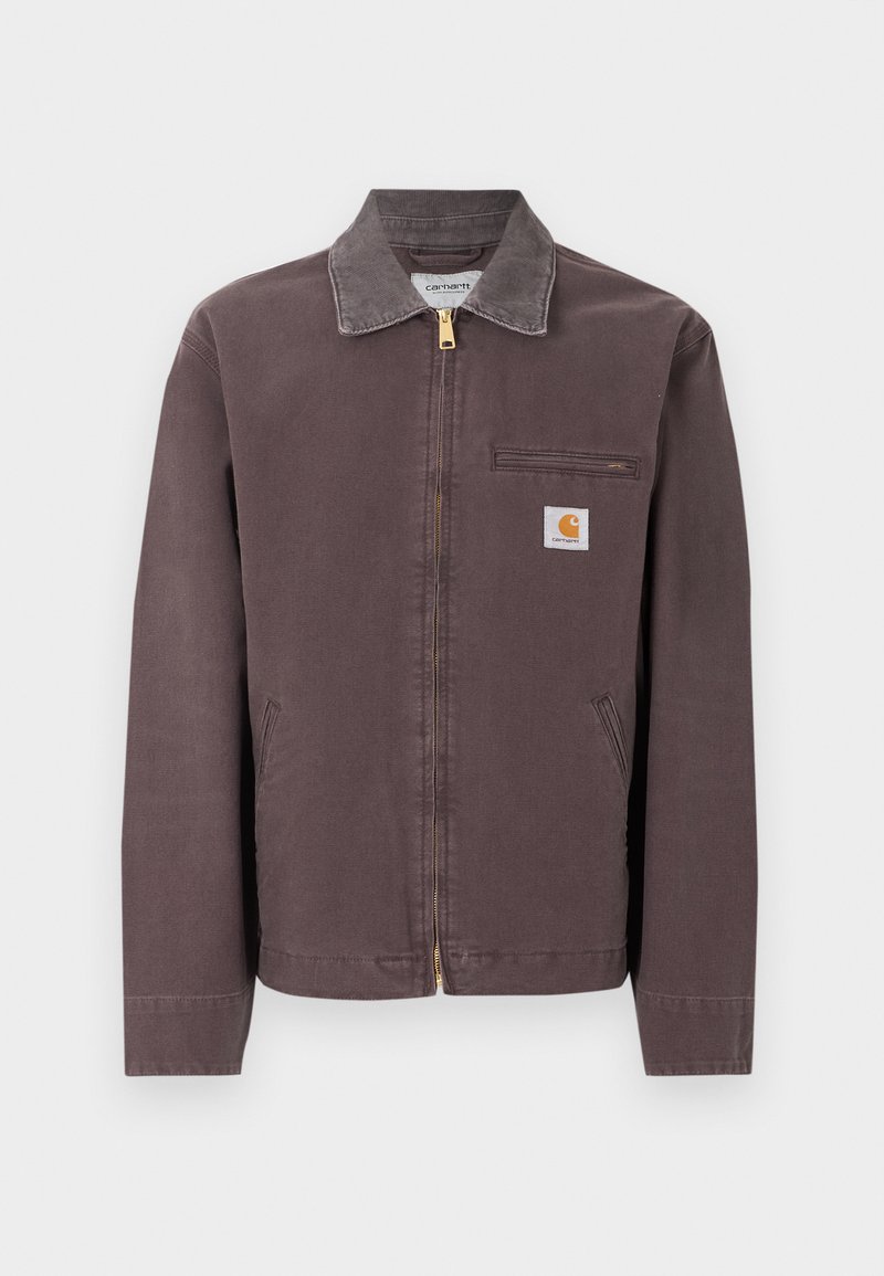 Chaqueta marrón con cremallera y cuello, bolsillo con cremallera en el pecho, dos bolsillos laterales y parche con el logo de Carhartt en el pecho izquierdo.