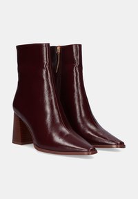 Botas de tobillo de cuero burdeos con un acabado brillante, punta afilada y un tacón de bloque de altura media, que cuentan con un cierre de cremallera lateral.