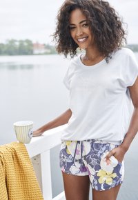 Lichtblauwe katoenen T-shirt met de opdruk "Soul full of sunshine", gecombineerd met bloemenshorts in paars, geel en wit. Gele gestructureerde stof in de buurt.
